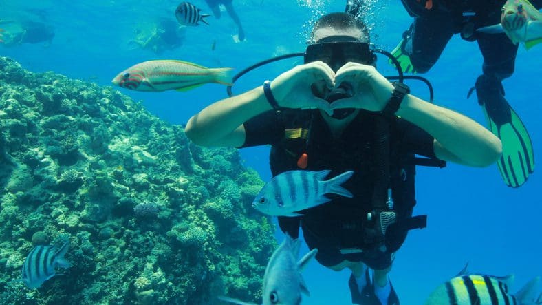 Scuba diver forming heart underwater with fish.